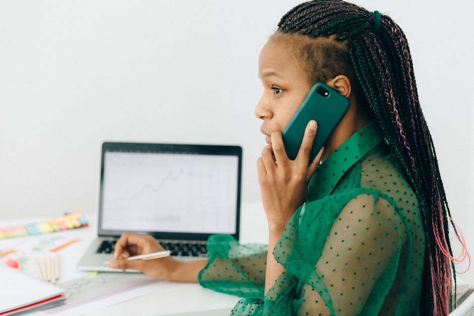 Focused woman engaged in remote work using a phone and laptop at an office desk