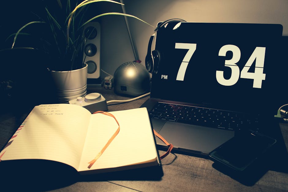 A cozy workspace with a laptop displaying time, open notebook, and headphones under warm lighting.