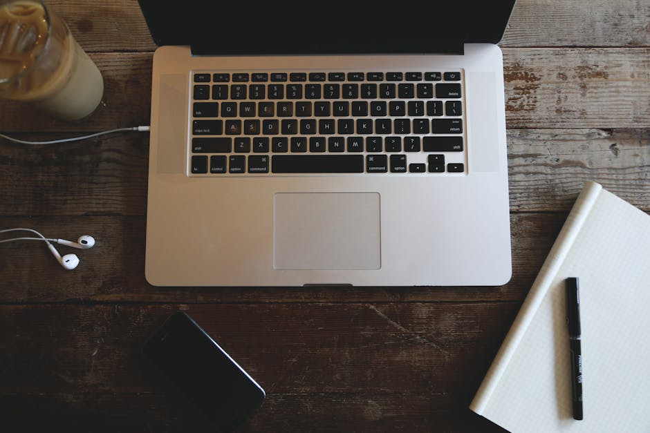 Top-down view of a laptop, headphones, notebook, and iced coffee on a wooden desk.
